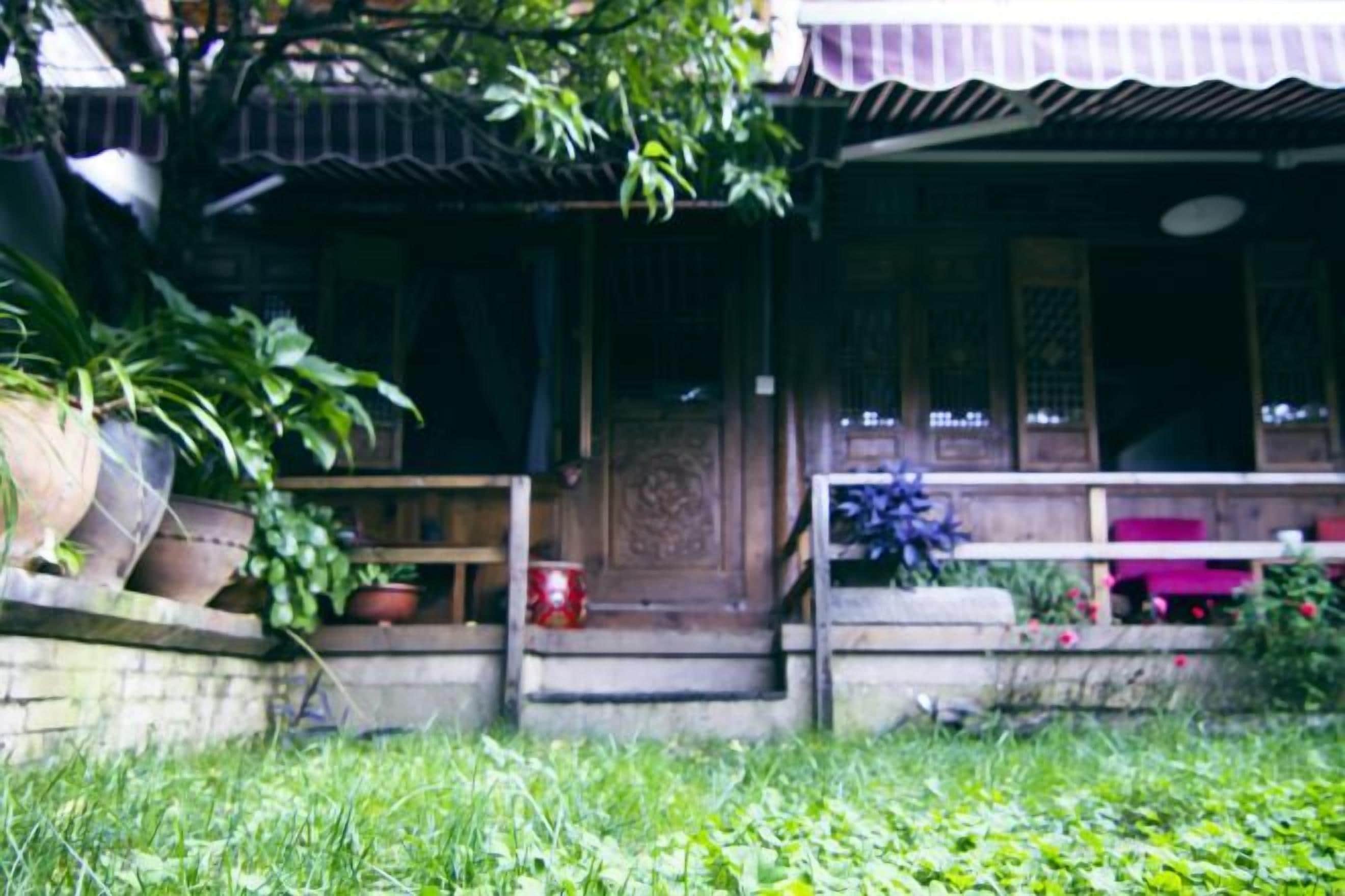 A traditional wooden house with a porch, steps leading to the entrance, and potted plants.
