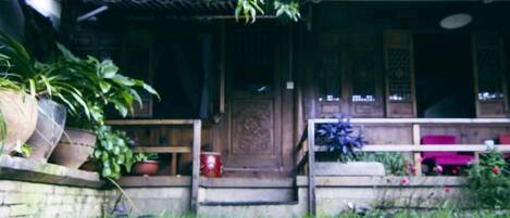 A traditional wooden house with a porch, steps leading to the entrance, and potted plants.