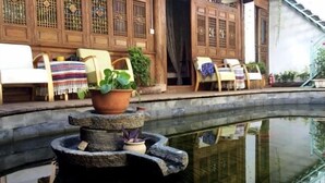 A traditional courtyard with a stone water feature, wooden furniture, and a building with intricate wooden lattice windows.