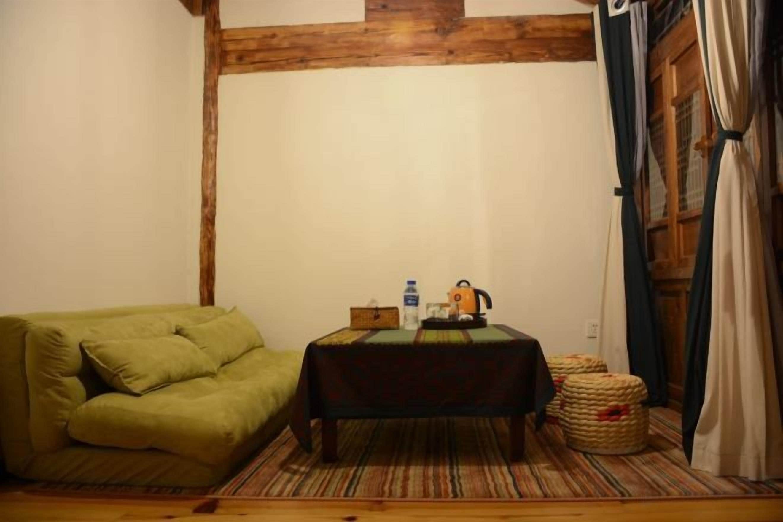A cozy room with a green sofa, a small table with a kettle, and a wooden floor.