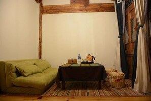 A cozy room with a green sofa, a small table with a kettle, and a wooden floor. - Mrs. Sha's Living Room Inn (Jianchuan)
