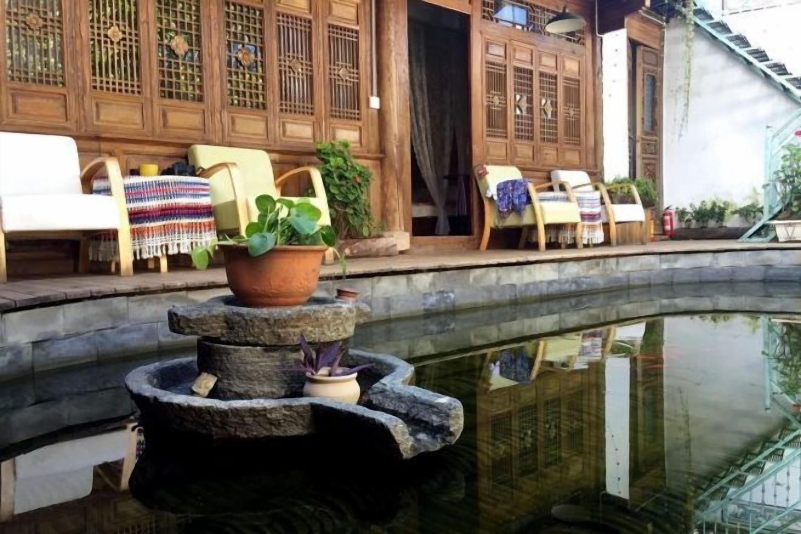 A traditional courtyard with a stone fountain, wooden furniture, and a reflection in the water.