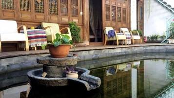 A traditional courtyard with a stone fountain, wooden furniture, and a reflection in the water.
