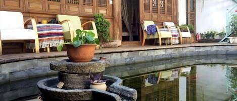A traditional courtyard with a stone fountain, wooden furniture, and a reflection in the water.