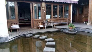 A traditional wooden building with a covered outdoor seating area, a small pond with stepping stones, and a potted plant.