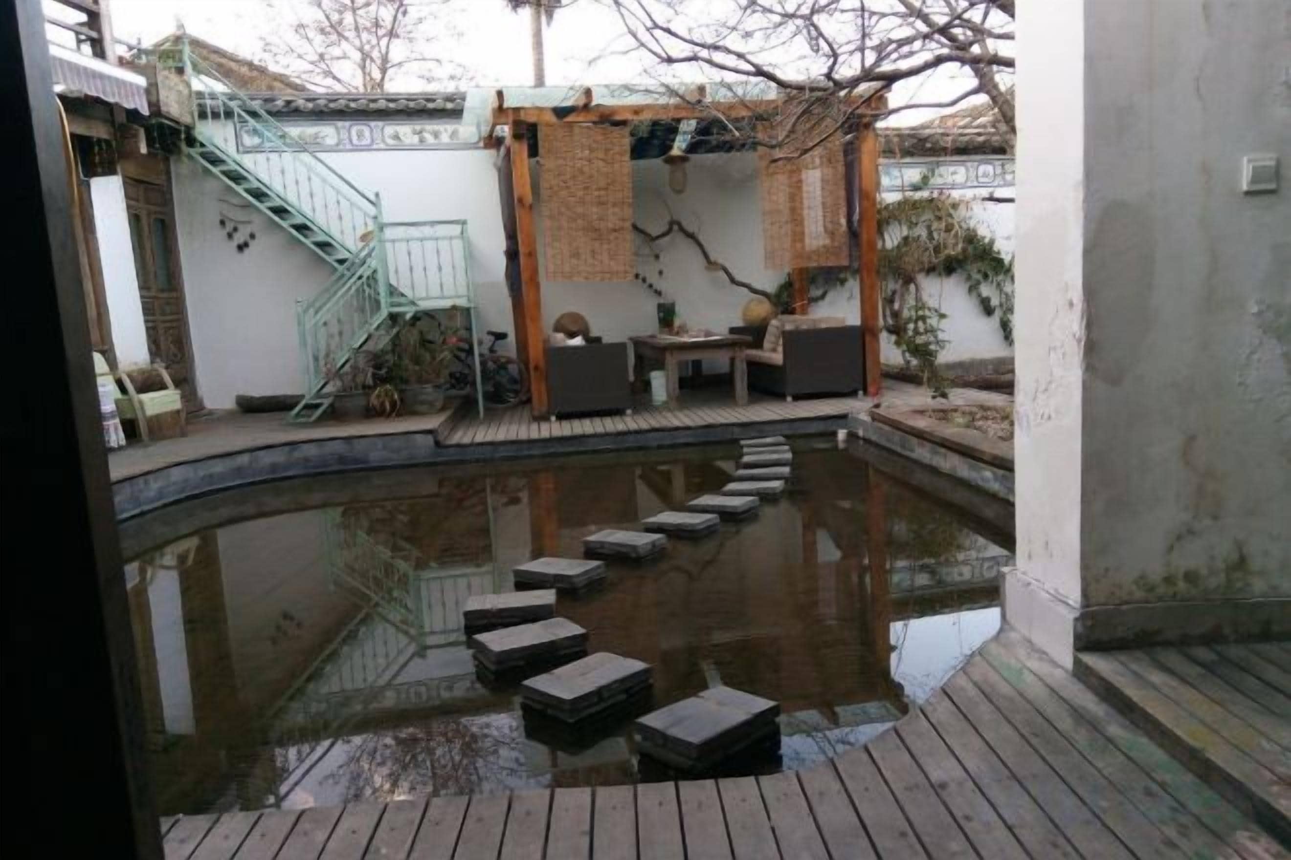 A courtyard with a wooden deck, a small pond with stepping stones, a covered seating area, and a staircase.