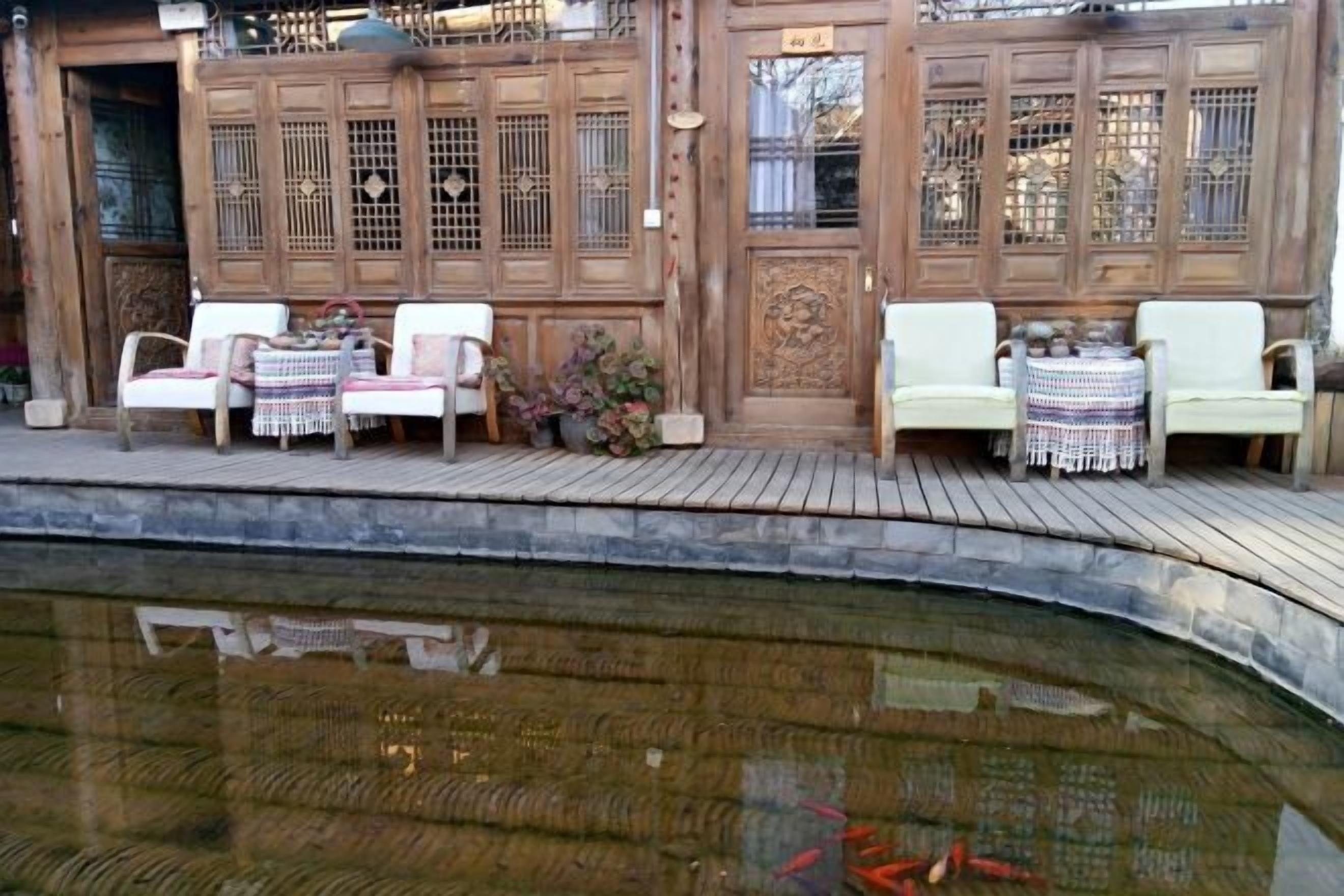 A traditional building with a wooden exterior, a pond in the foreground, and outdoor seating with tables and chairs.