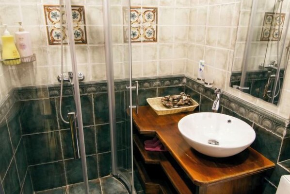 Un baño con ducha envuelta en cristal, tocador de madera con lavabo y azulejos decorativos en las paredes.