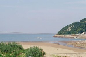 A beach with a sandy shore, a small boat, and a hill with vegetation. - Peach blossom island bay longines farmhouse (Zhoushan)