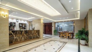 A hotel lobby with a marble reception desk, a dining area with a table and chairs, and a large chandelier. - Qihupan Inn Heping (Wuxi)