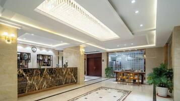 A hotel lobby with a marble reception desk, a chandelier, and a reception area with a wooden counter.
