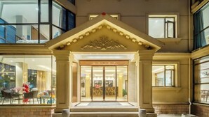 A hotel entrance with a grand archway, glass doors, and a brick-paved area with steps leading up to the entrance. - Qihupan Inn Heping (Wuxi)