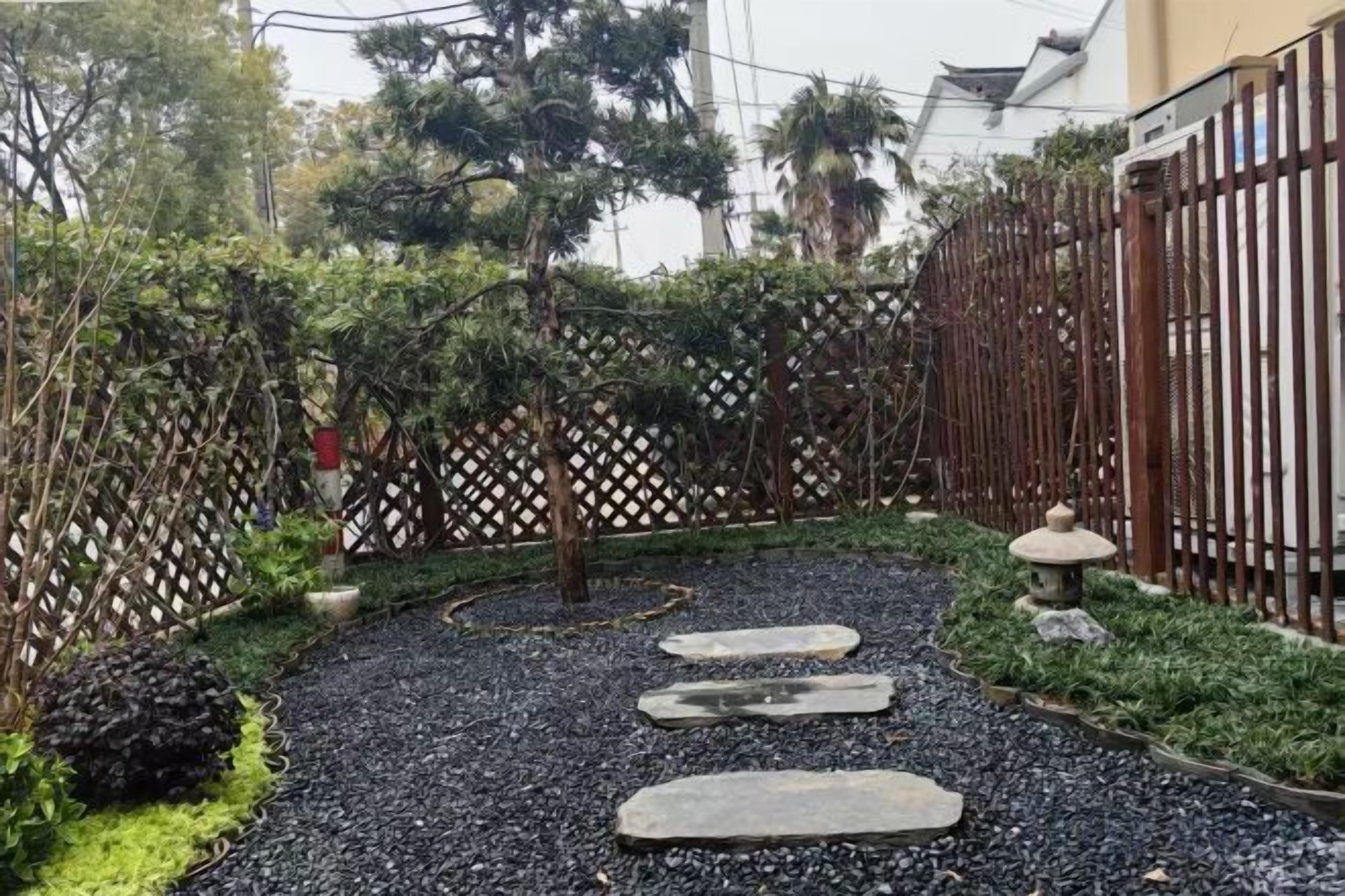 A garden pathway with stepping stones, surrounded by greenery and a decorative fence.