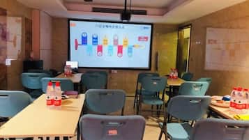 Un salón de conferencias con una pantalla de proyector mostrando una presentación, varias mesas con sillas y botellas de agua sobre las mesas.