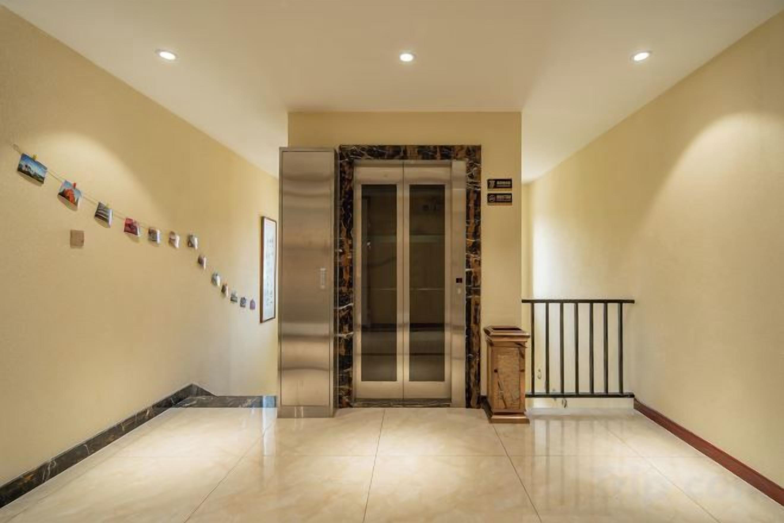 A hotel corridor with a marble floor, an elevator, a wooden cabinet, and a black railing.