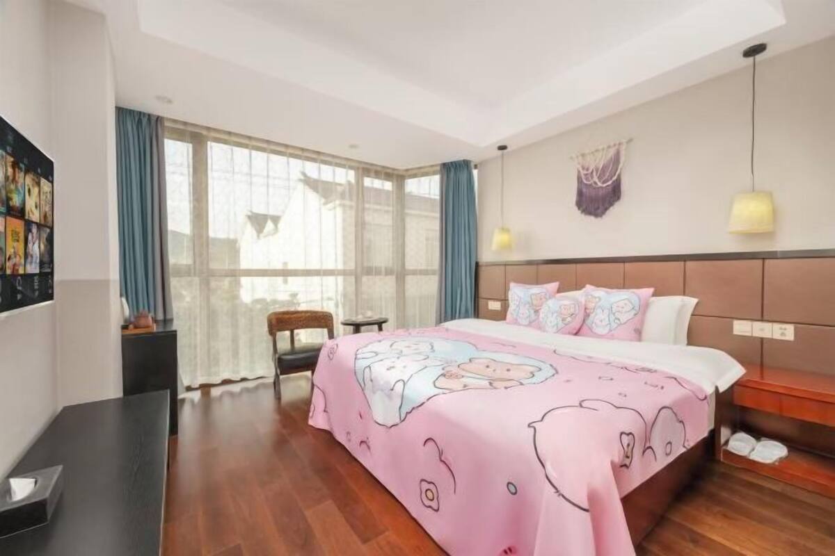 Quarto com cama, escrivaninha, cadeira, janela com cortinas e luminária na parede.