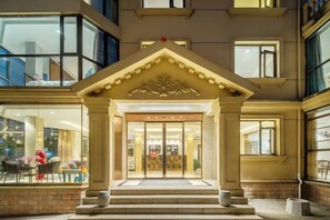 Entrada de hotel con un arco imponente, una escalera que conduce al mismo y un gran escaparate de vidrio.