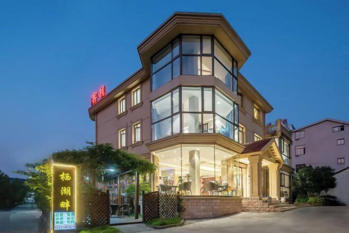 Hotel com fachada de vidro, área externa com mesas e cadeiras e um letreiro com caracteres chineses.