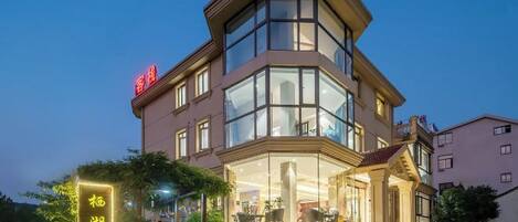 A corner hotel with a glass facade, a visible outdoor seating area, and a sign with Chinese characters.