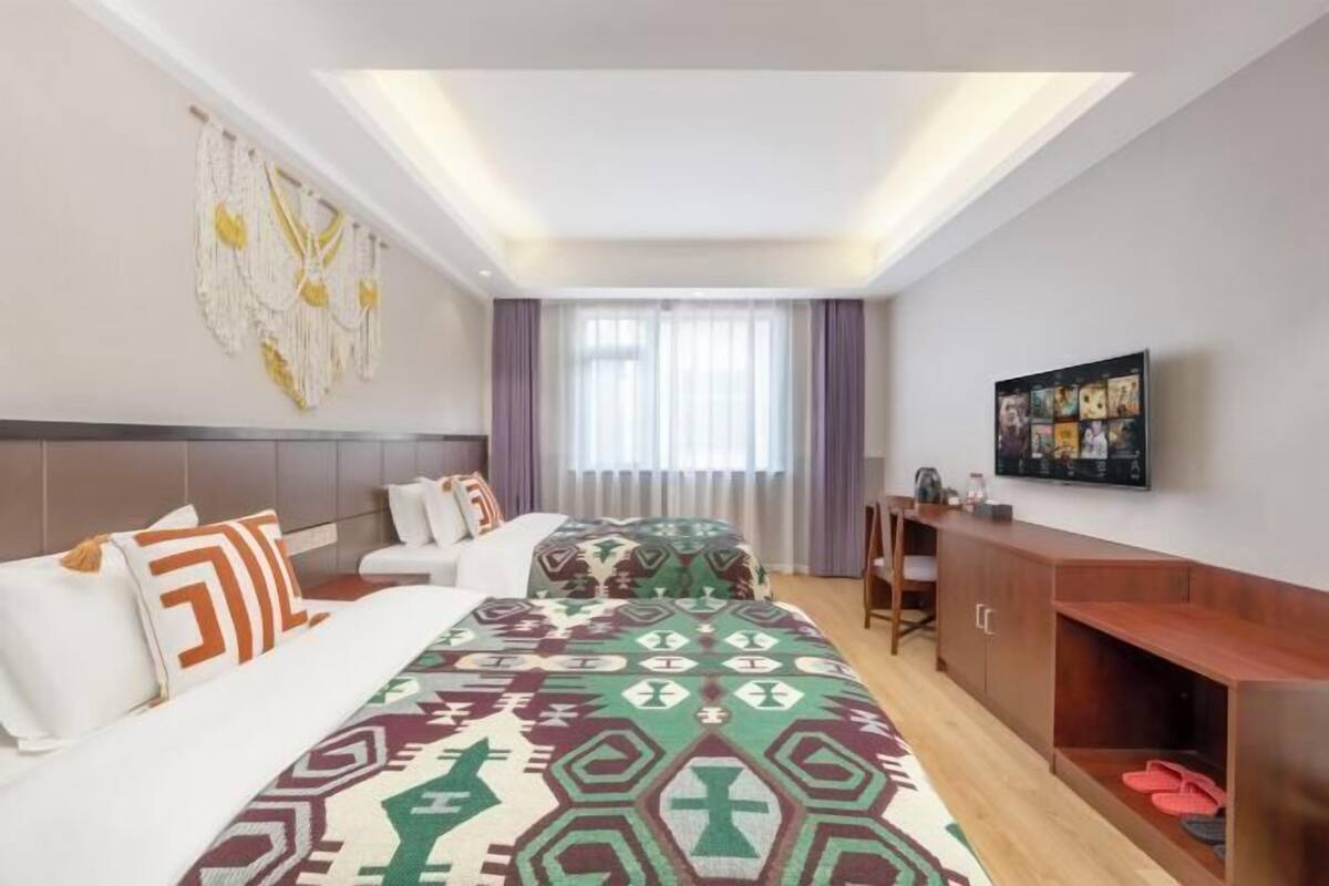 Quarto de hotel moderno com cama, escrivaninha, TV e janela com cortinas.