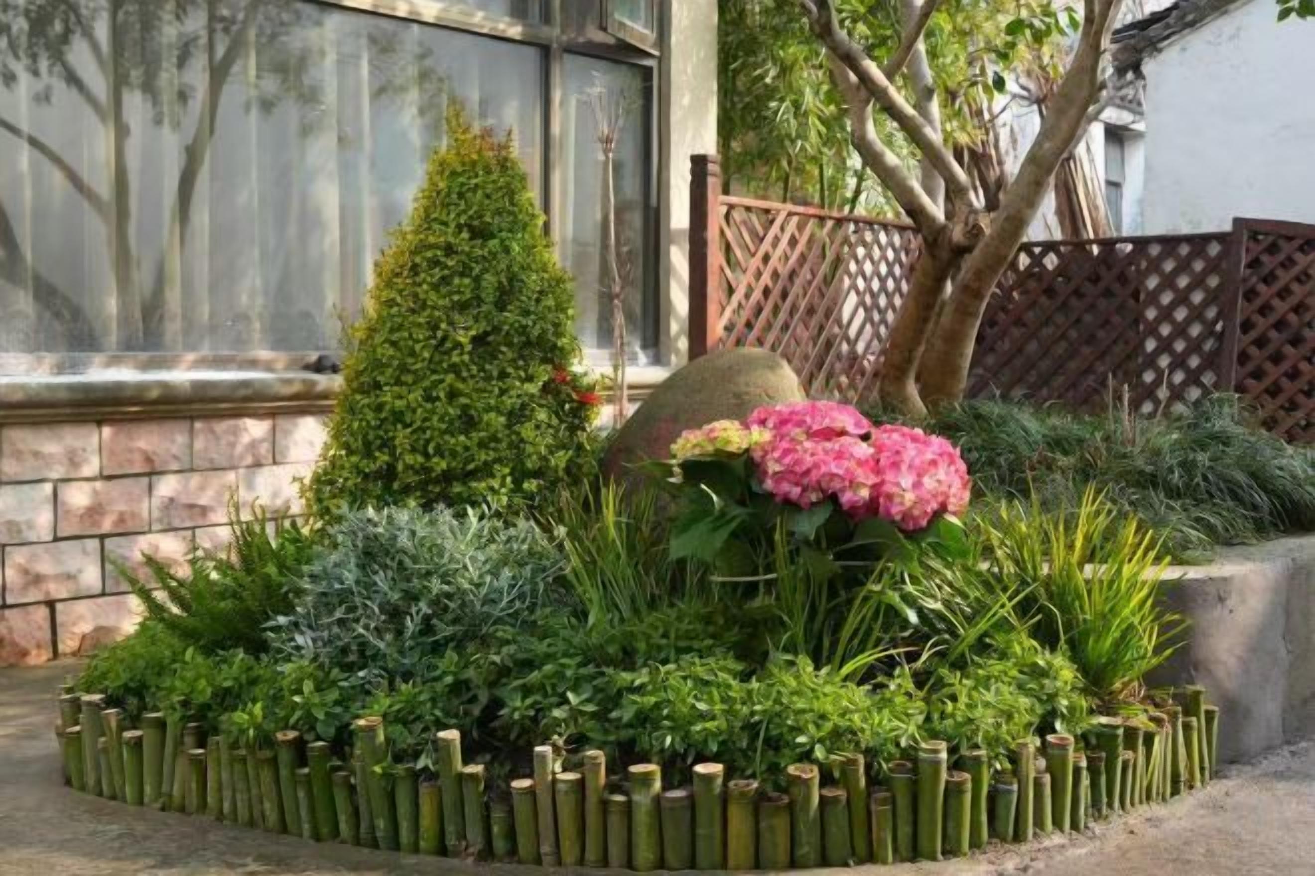 A landscaped garden with a variety of plants, a decorative rock, and a bamboo fence.