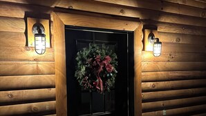 L’entrée d’un chalet en bois, avec une porte noire, une couronne décorative et deux lampes fixées au mur.
