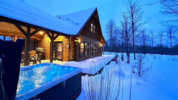 Une cabane en rondins dotée d’un bain à remous et d’une terrasse couverte.