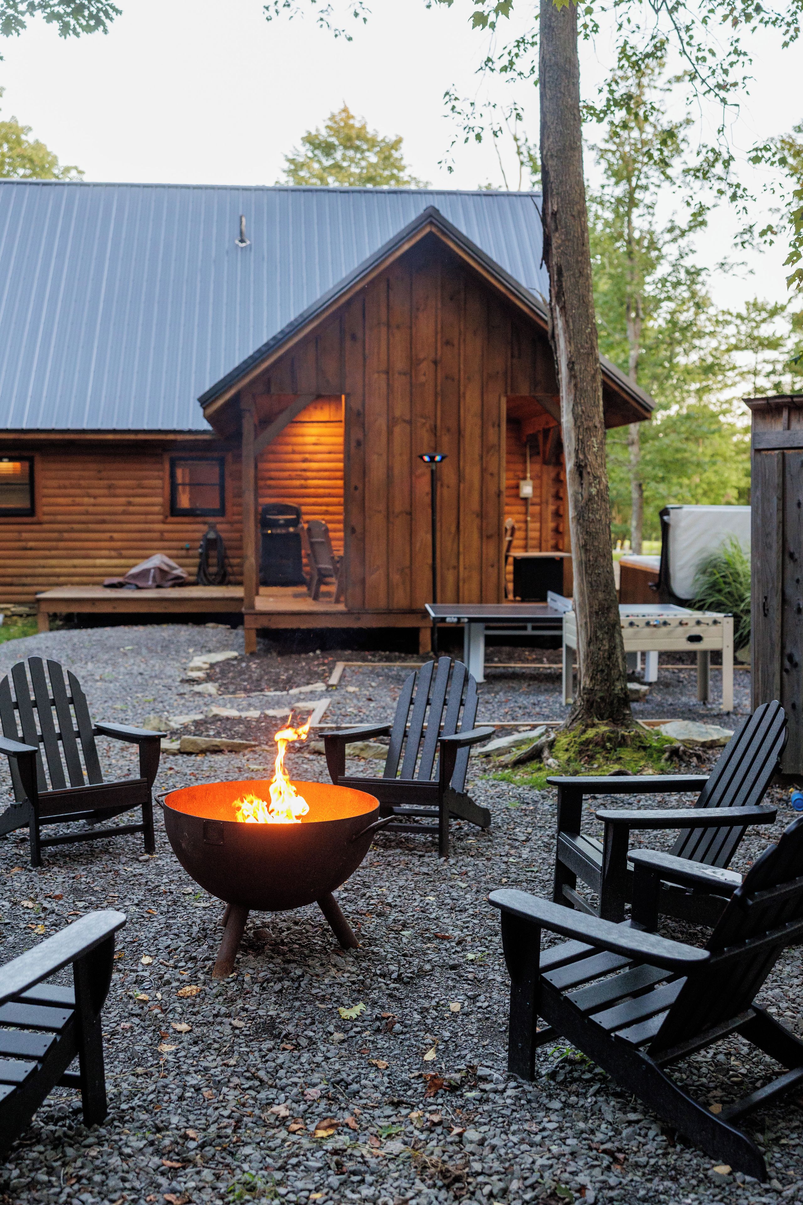 Une cabane en bois avec un foyer au centre, entourée de fauteuils Adirondack.