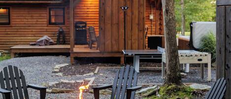 A wooden cabin with a fire pit in the center surrounded by Adirondack chairs.