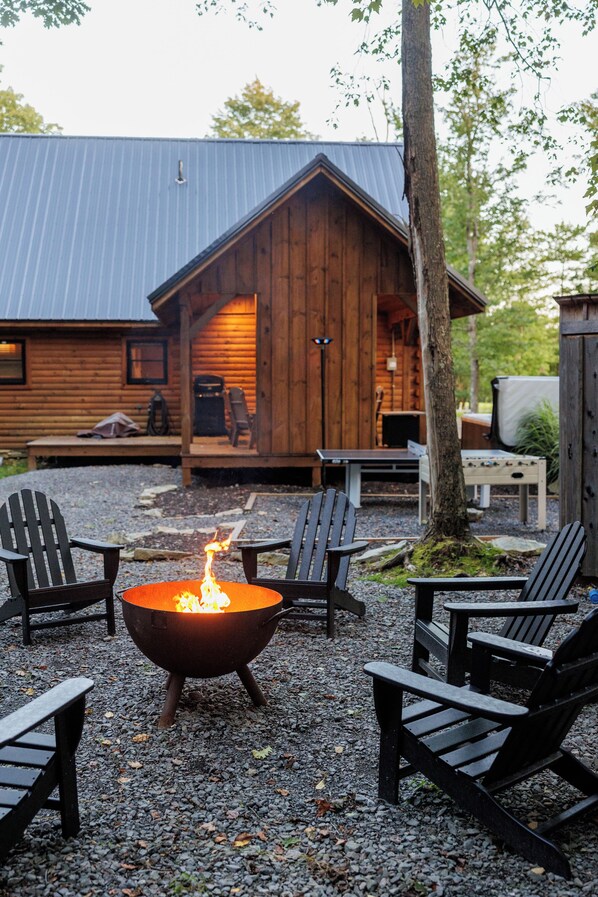 Une cabane en bois avec un foyer au centre, entourée de fauteuils Adirondack.