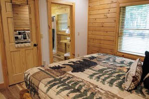 Une chambre avec une porte en bois, un lit recouvert d’une couvre-lit à motifs de camouflage et une fenêtre avec des stores.
