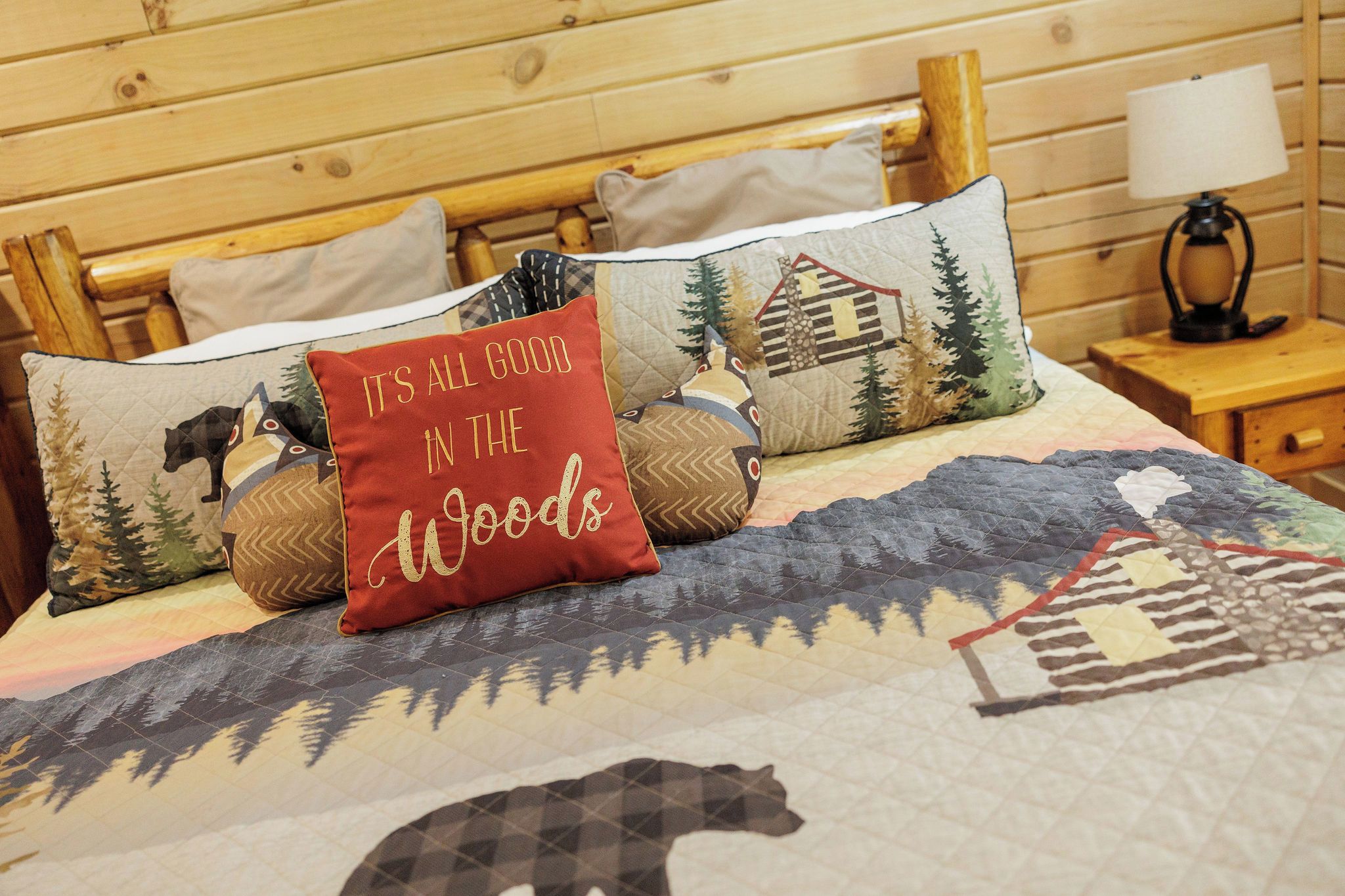 Una cama con colcha adornada con motivos de bosque y fauna, rodeada por un cabecero de madera y almohadas con diferentes diseños.