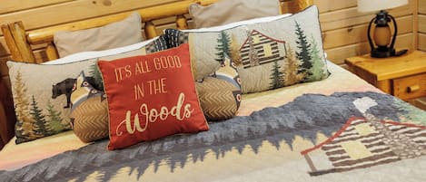 Una cama con colcha adornada con motivos de bosque y fauna, rodeada por un cabecero de madera y almohadas con diferentes diseños.