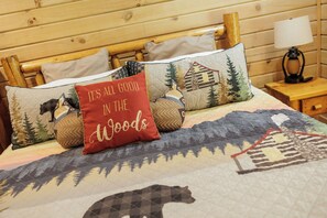 Una cama con colcha adornada con motivos de bosque y fauna, rodeada por un cabecero de madera y almohadas con diferentes diseños.