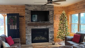 Un salon chaleureux avec une cheminée en pierre, un téléviseur à écran plat et un sapin de Noël.