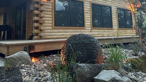 Une cabane en rondins dotée d’une grande terrasse, d’une cheminée en pierre et d’un mur de pierre en premier plan.