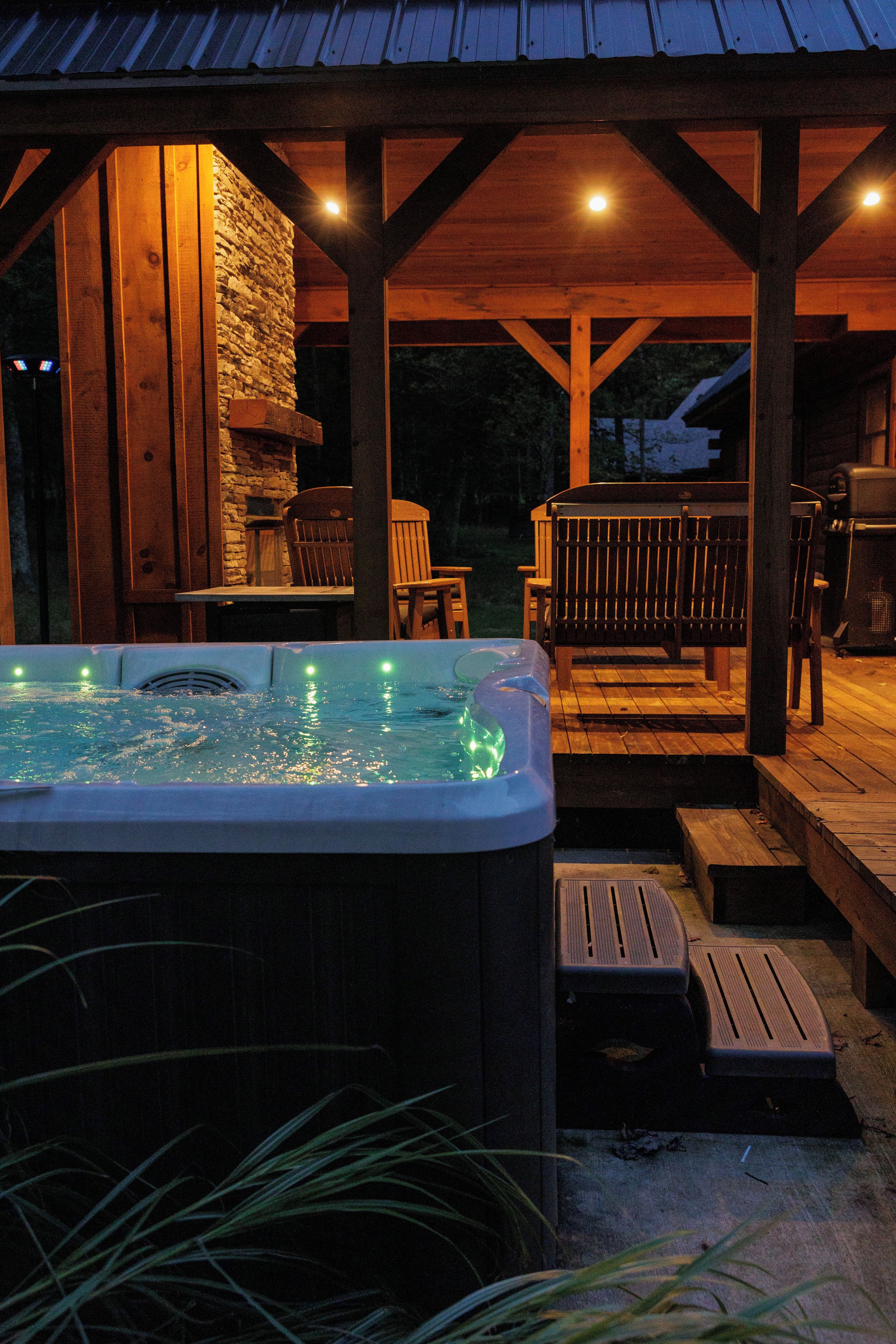 A hot tub with a stone wall and wooden deck, surrounded by outdoor furniture.