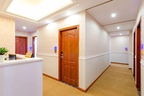 A hotel hallway with a reception desk, wooden doors, and a carpeted floor.