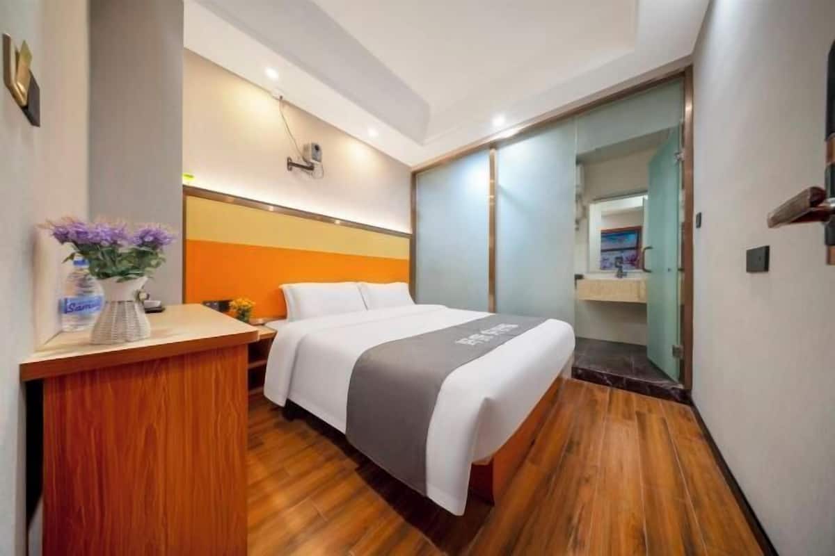 Una habitación de hotel con una cama, un escritorio de madera, un florero con flores y un espejo.