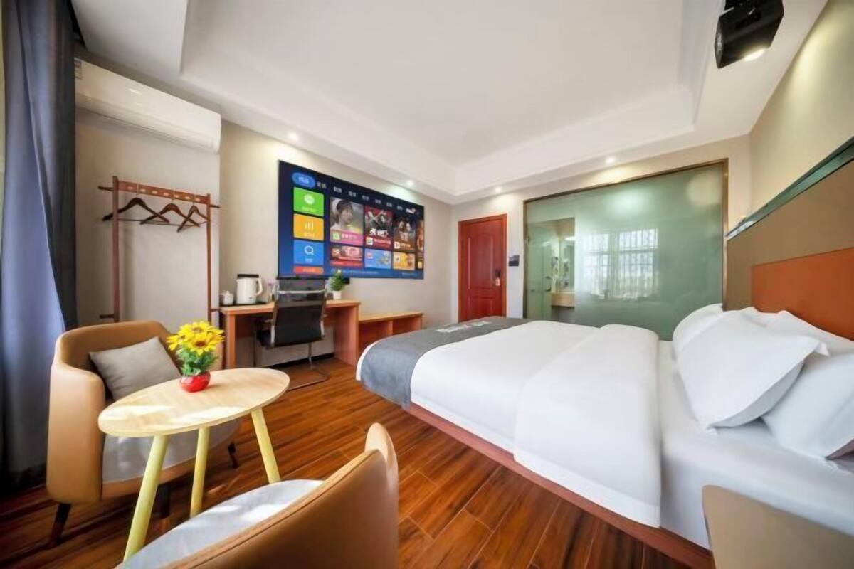 Habitación de hotel con cama, escritorio, silla, una pequeña mesa con un florero y televisor montado en la pared.