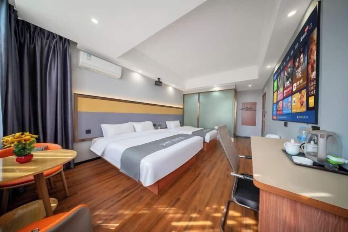 Habitación de hotel con cama, escritorio, silla, mesa con flores y una pared con pantalla mostrando contenido.