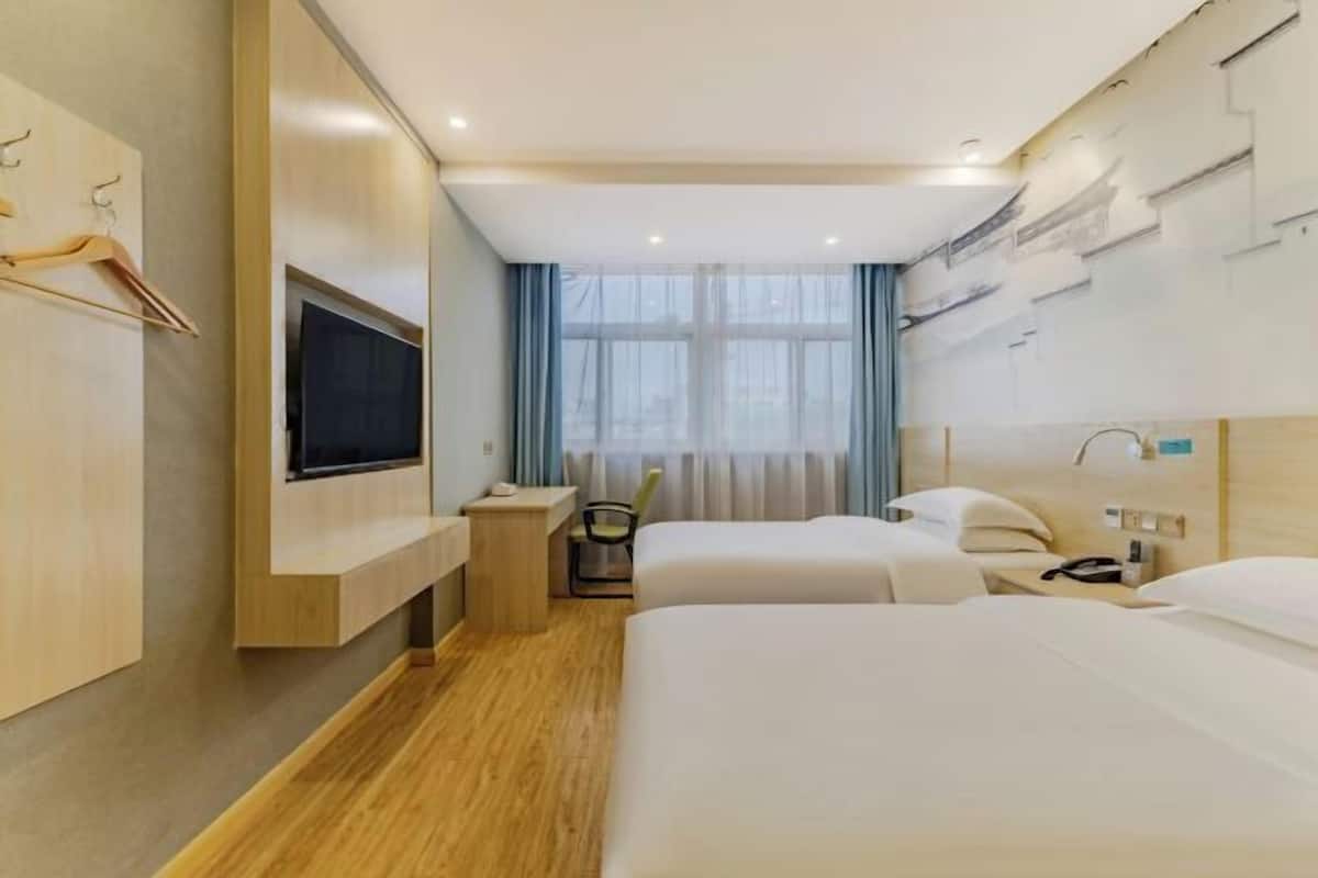 Habitación de hotel con dos camas, un televisor montado en la pared, un escritorio y una silla.