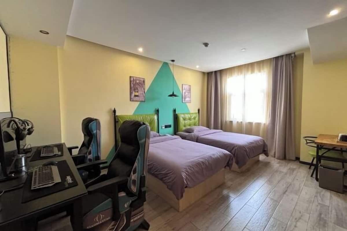 Habitación de hotel con dos camas, un escritorio con computadora, una silla y una pequeña mesa.