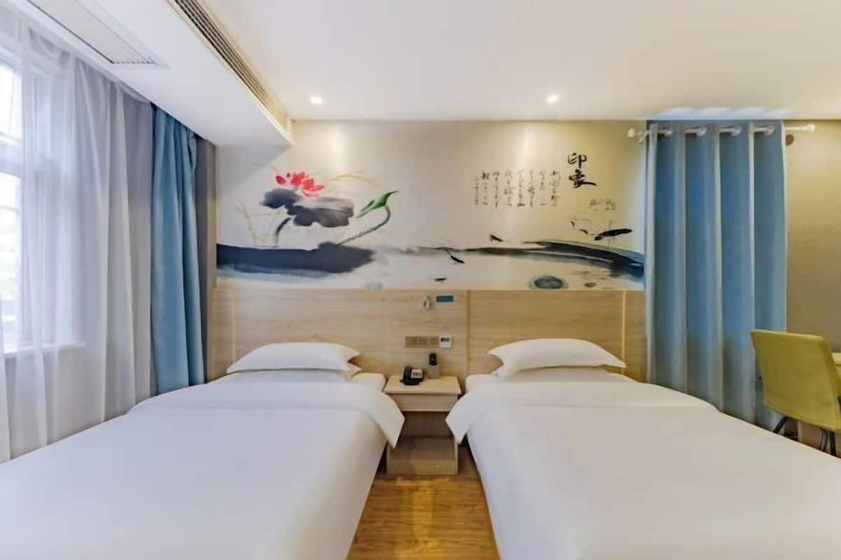 Habitación de hotel con dos camas, un escritorio, una silla y una pared con una pintura y caligrafía.