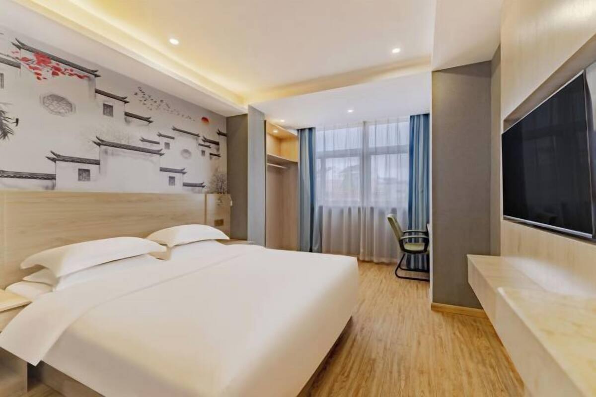 Habitación de hotel con una cama grande, un televisor montado en la pared, un cabecero de madera y una pared decorativa con motivos tradicionales.