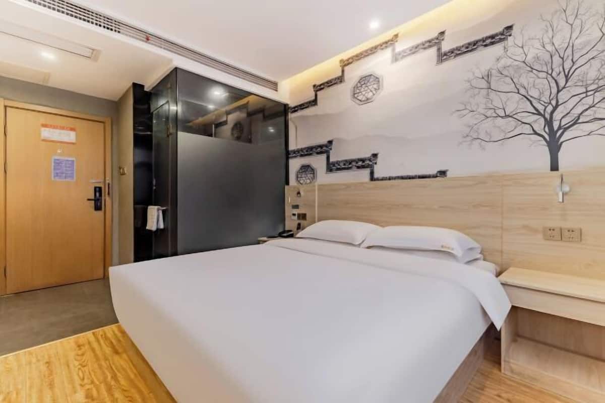 Una habitación de hotel moderna con una cama grande, cabecera de madera, armario empotrado y televisor de pared.