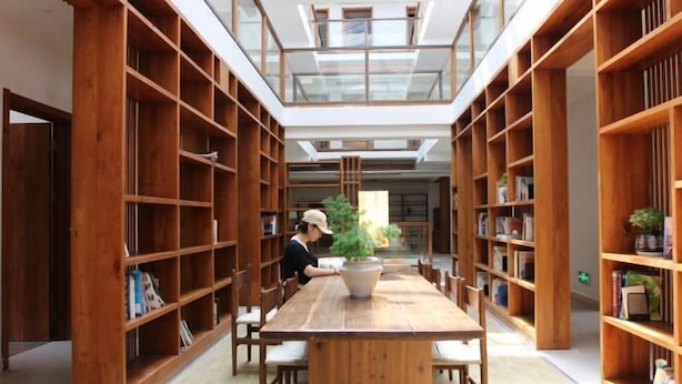 A modern library interior with wooden bookshelves, a central table, and a skylight. - Bishan Banshe Holiday Villa (Xianju)