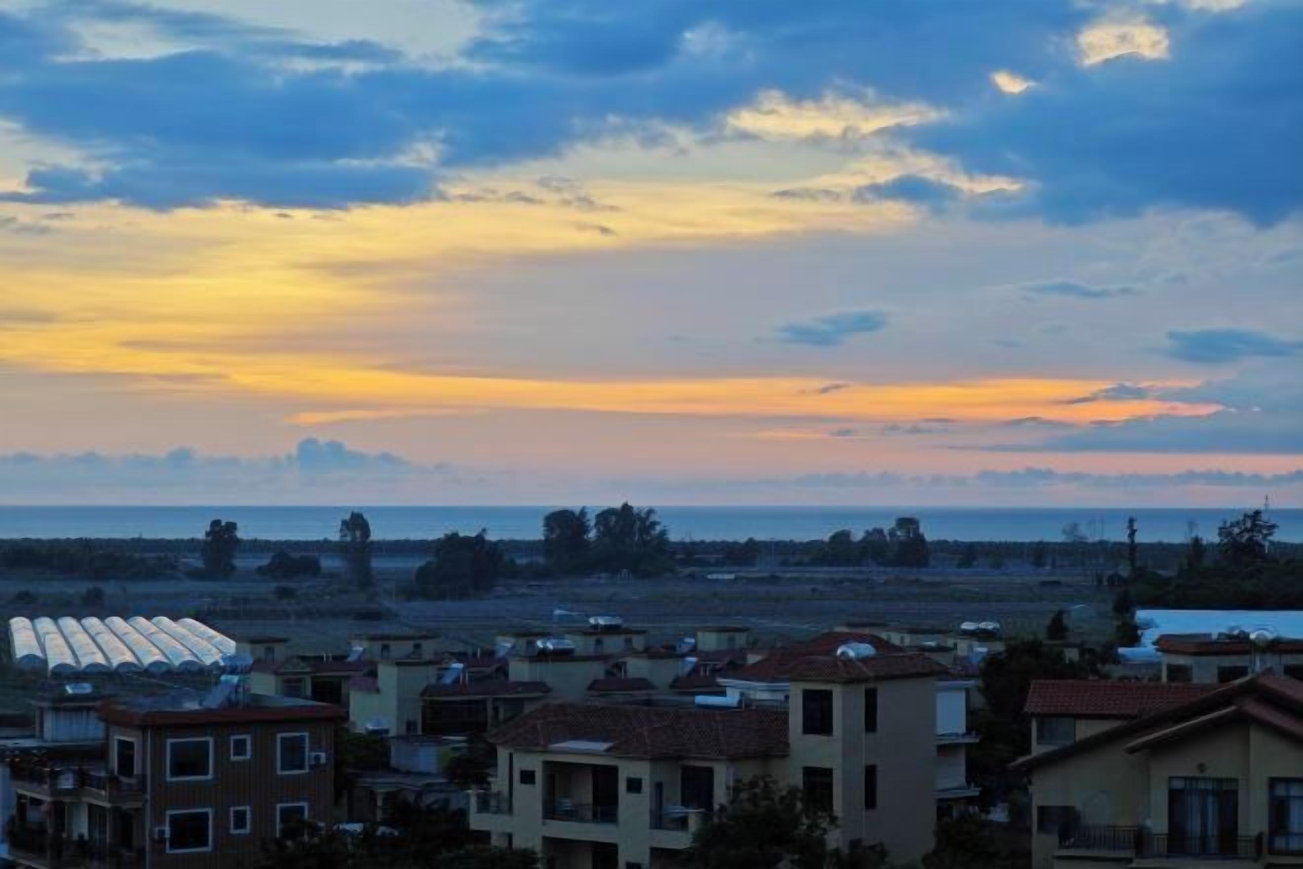 A residential area with houses and a distant view of the sea at sunset.