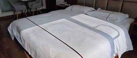Una cama grande con ropa blanca y un cabecero, una mesita con sillas y un reloj sujeto a la pared.