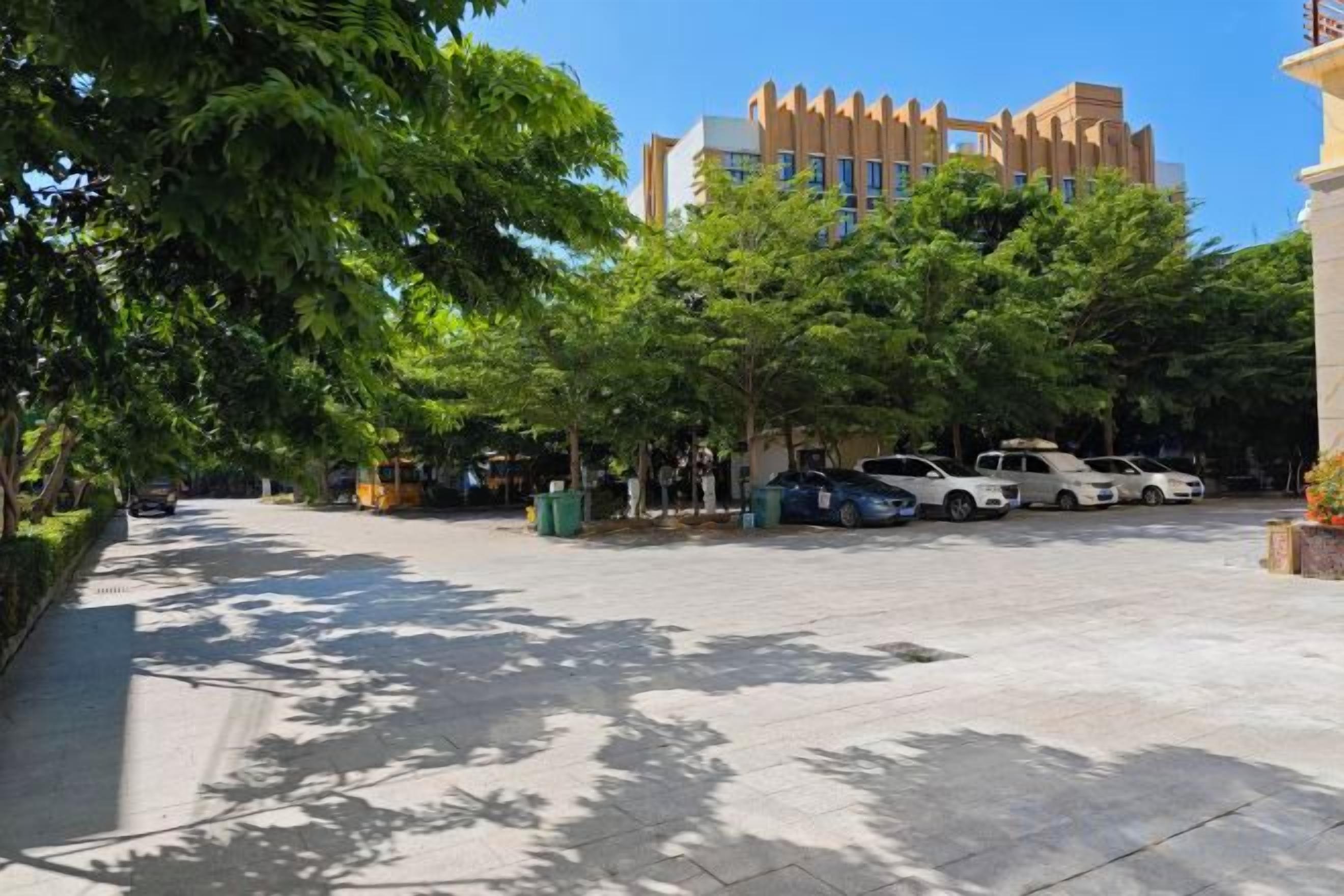 Un estacionamiento con árboles y un edificio al fondo.